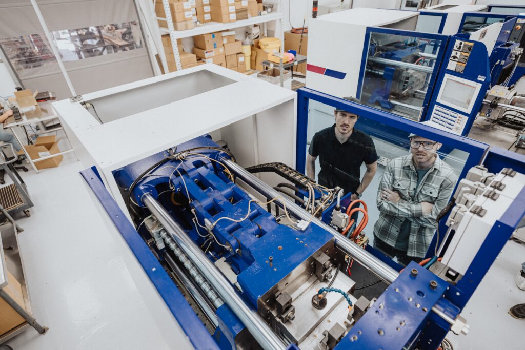 High angle view looking down at two men working in a manufacturing and fabrication facility examining a plastic injection molding machine in a clean room.
