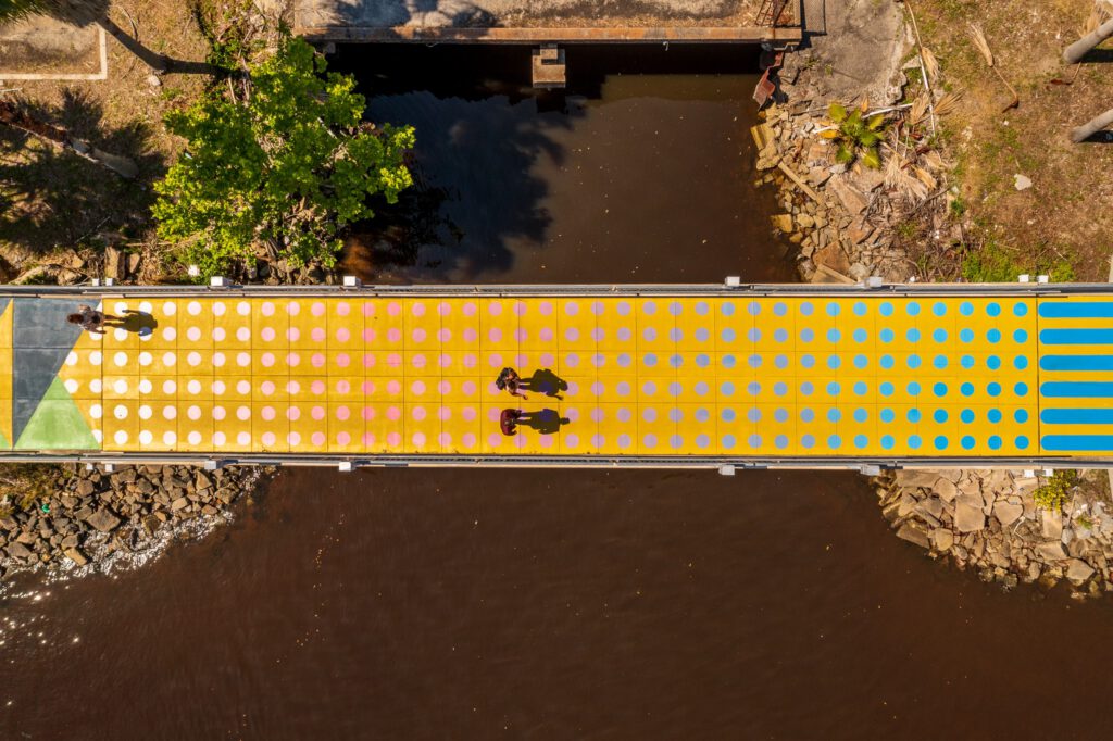 Three people cross an artful bridge, arial view.