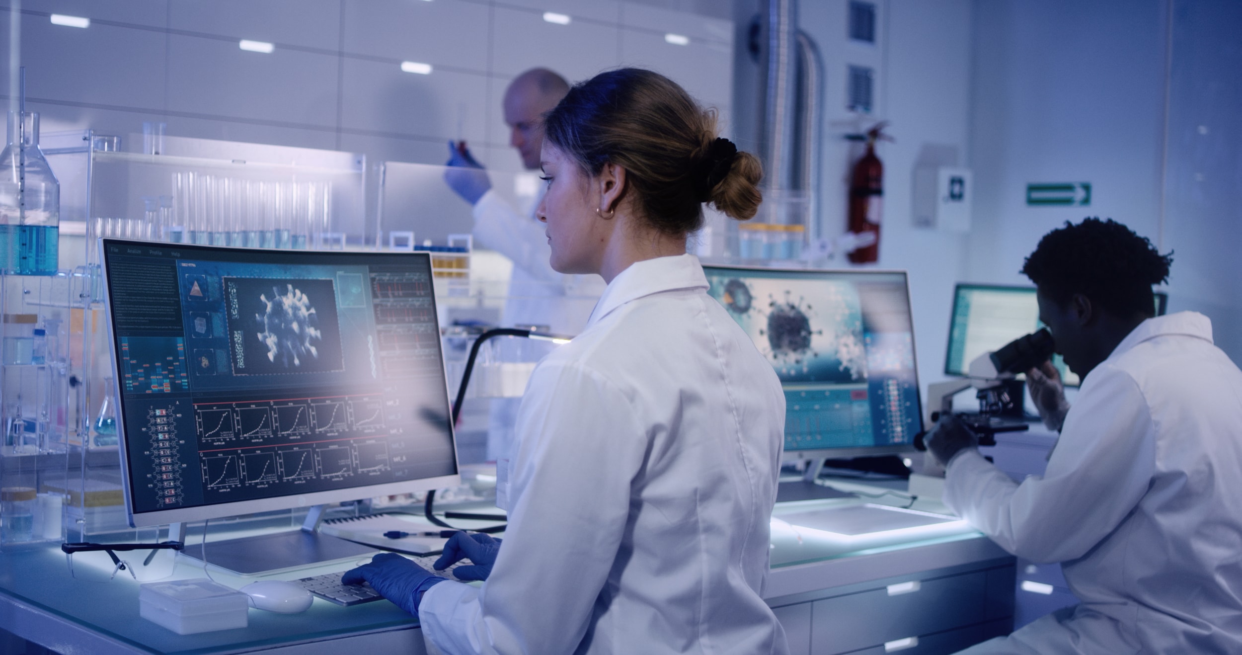 Young team conducting lab tests, Man in background using microscope