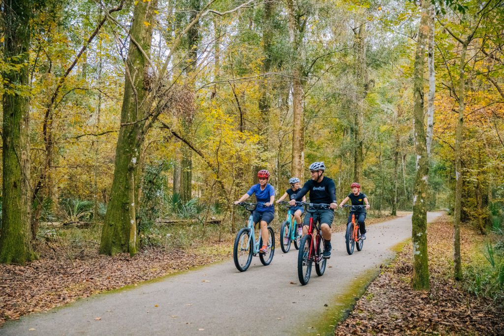 A family of bikers with helmets navigates a bike trail in the woods of Jacksonville.