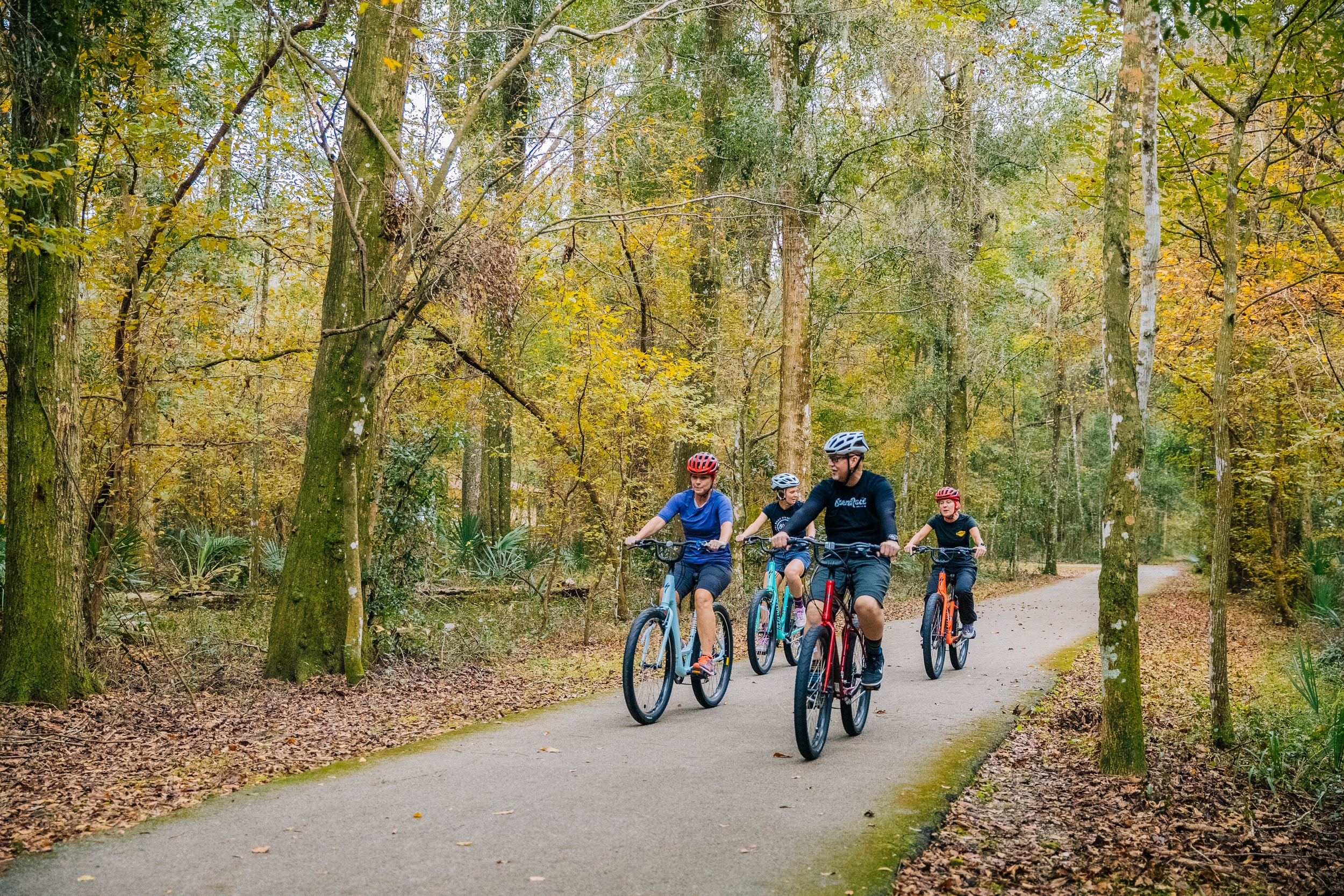 A family of bikers with helmets navigates a bike trail in the woods of Jacksonville.