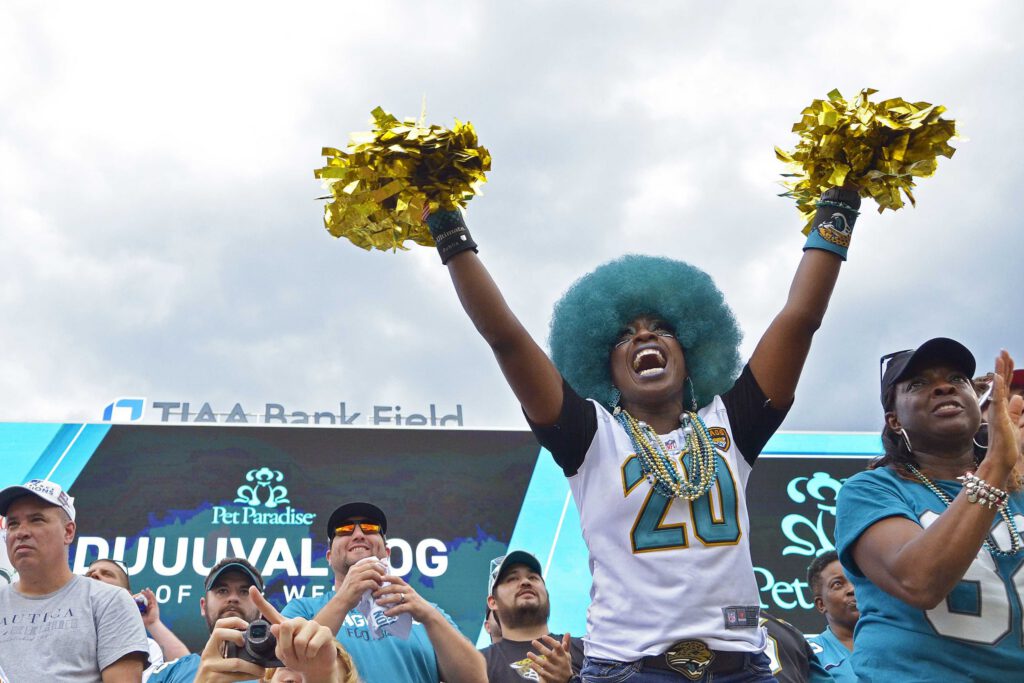 An excited Jaguars fan cheers with gold pop-poms during a game.