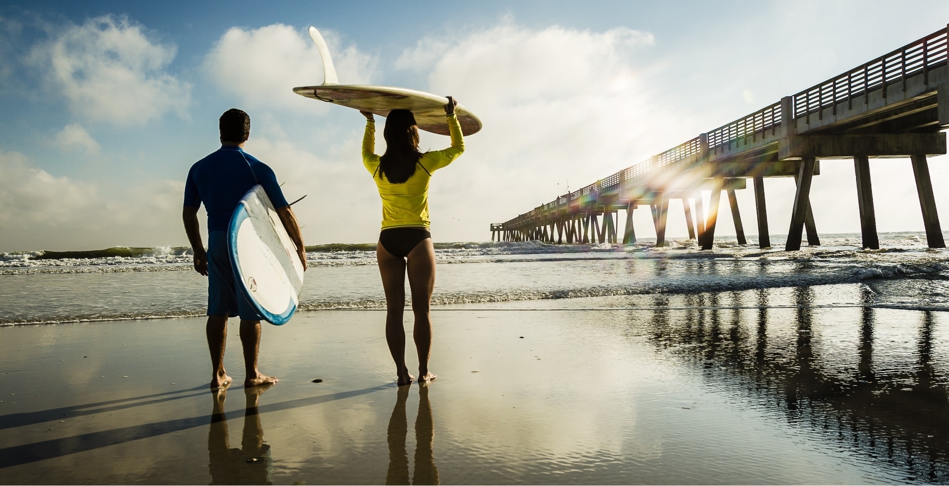 Two surfers enter the ocean at sunrise.