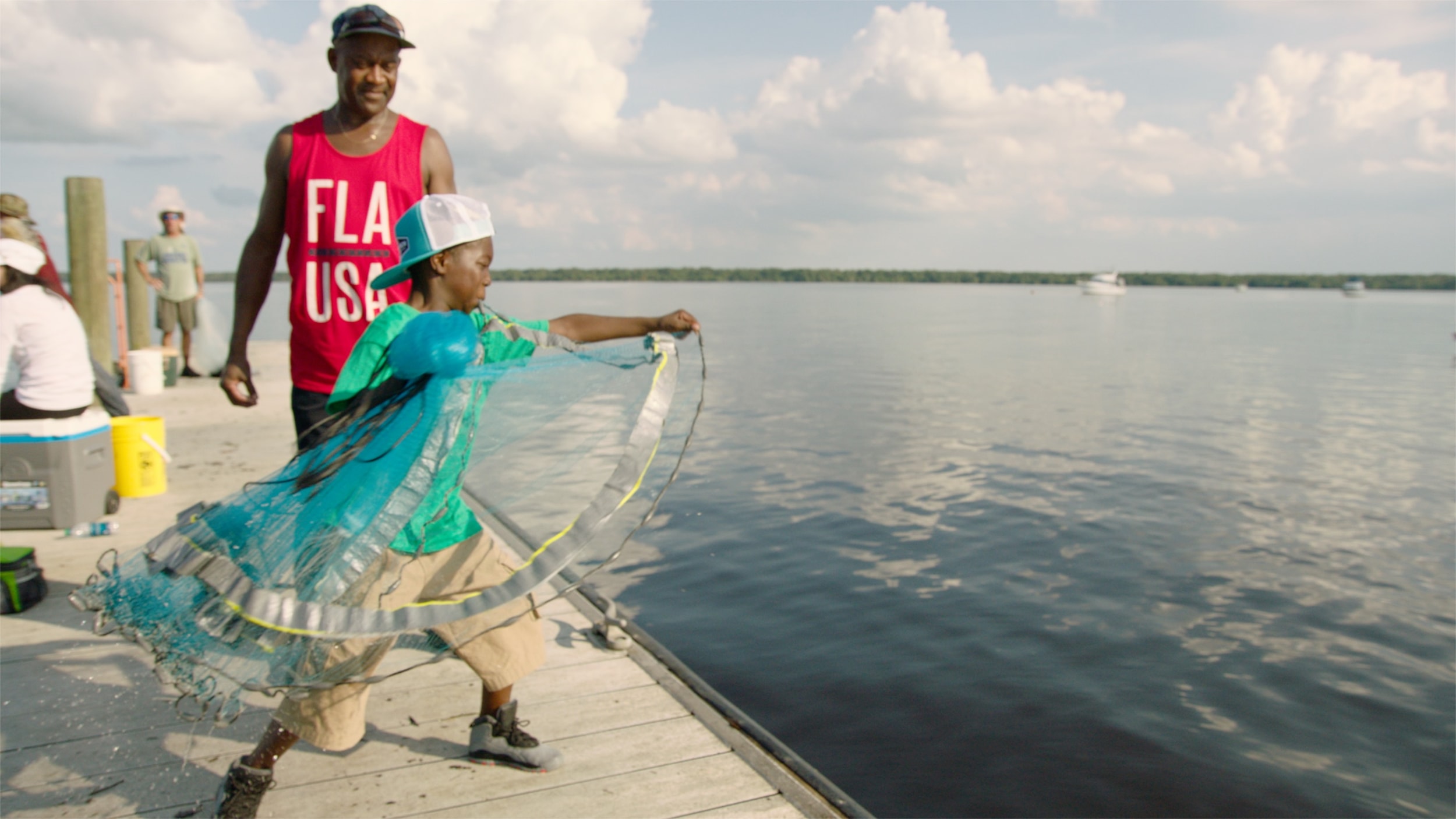 A child plays with a kite alongside his father on a dock.