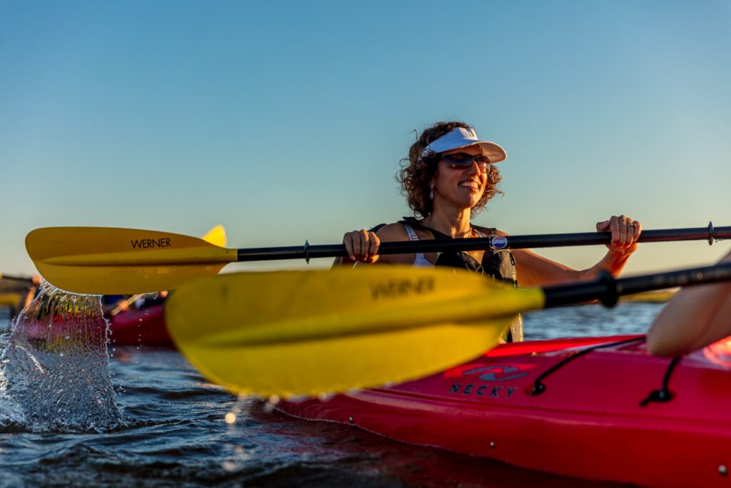 A happy woman kayaks, the photo focused on her oar.