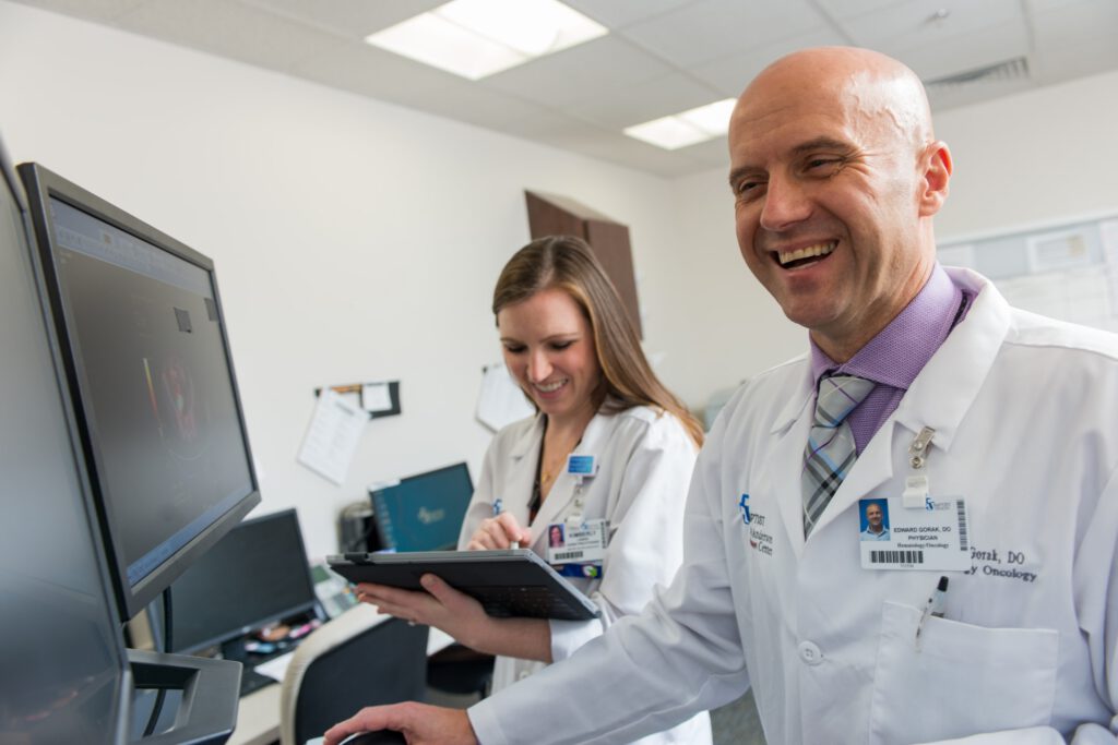 Two healthcare workers smile while reviewing a clipboard.