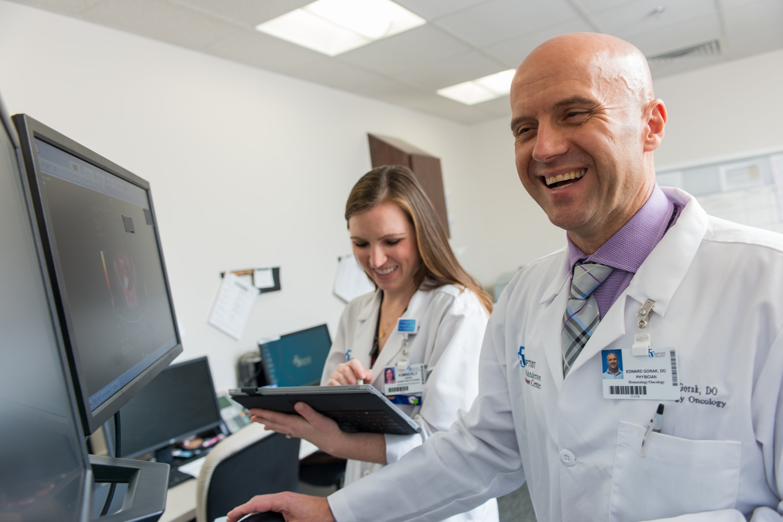 Two healthcare workers smile while reviewing a clipboard.